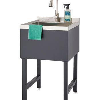 A freestanding black utility sink with a stainless steel basin and a brushed nickel gooseneck faucet is shown. A green dishcloth hangs over the front edge of the basin, and a spray bottle of cleaner sits on the back right corner of the sink.