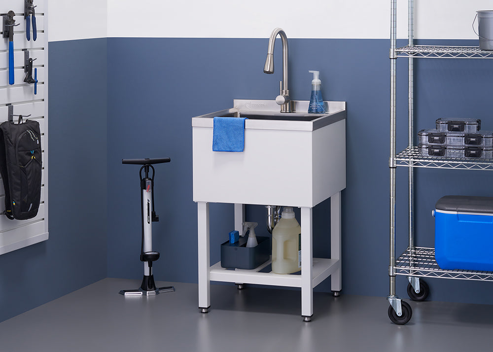A well-organized utility room features a white utility sink with a brushed nickel faucet and a blue hand towel hanging from the basin. To the left is a bicycle pump, and to the right, a metal shelving unit holds various storage containers and a blue cooler.