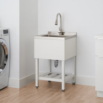 A modern white laundry room features a stainless steel utility sink with a white cabinet base and exposed silver legs. To the left, a large, silver front-loading washing machine sits next to a stack of folded towels.
