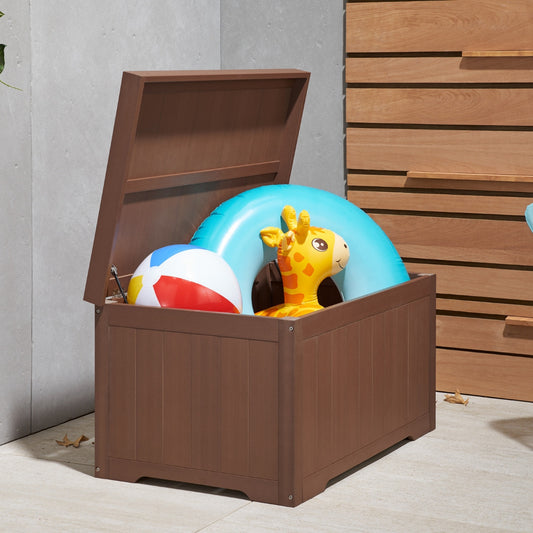 A brown outdoor deck box with a partially open lid is filled with colorful pool toys. Inside, a red, white, and blue beach ball, a light blue inflatable swim ring, and an inflatable yellow giraffe float are visible.
