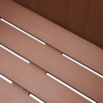 A close-up shot shows the textured, amber brown planks of an outdoor deck box, likely made of wood-plastic composite (WPC). The planks run diagonally across the frame, separated by thin white gaps that create a slatted appearance.