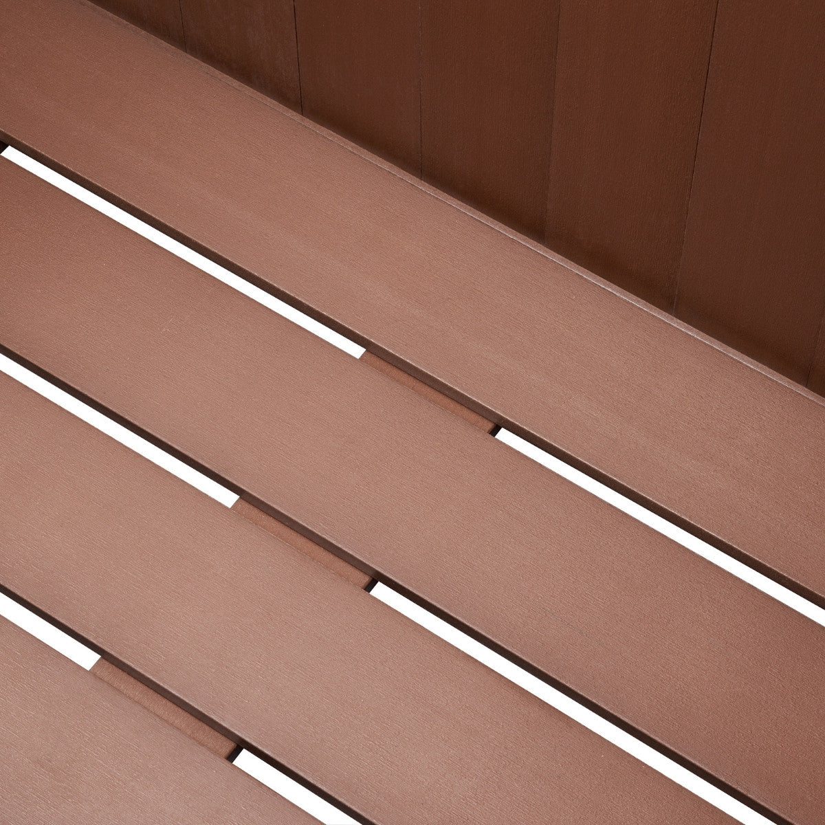 A close-up shot shows the textured, amber brown planks of an outdoor deck box, likely made of wood-plastic composite (WPC). The planks run diagonally across the frame, separated by thin white gaps that create a slatted appearance.