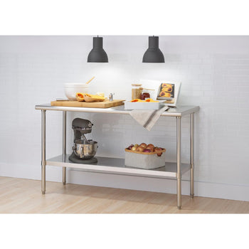 A stainless steel kitchen prep table with two shelves stands against a white tiled wall. The top shelf holds various kitchen items including a stand mixer, cutting board with butternut squash, bowls, and a cookbook, while the bottom shelf holds a basket of onions.