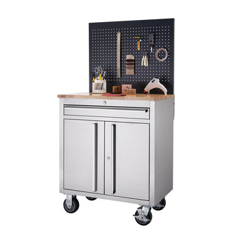 A stainless steel workbench with a light-colored wooden top stands on four black wheels. Above the workbench is a black pegboard with various tools and supplies hanging on it.