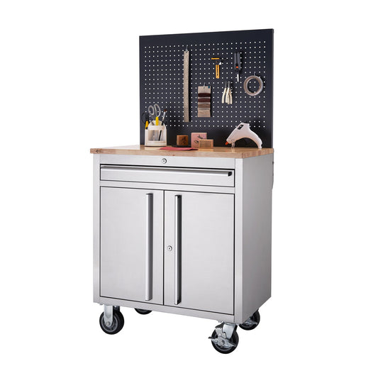A stainless steel workbench with a light-colored wooden top stands on four black wheels. Above the workbench is a black pegboard with various tools and supplies hanging on it.
