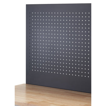 A close-up shows a section of a wooden workbench with a dark gray pegboard rising vertically from its surface. The pegboard is evenly perforated with numerous small, round holes arranged in a grid pattern.