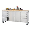 A 72-inch stainless steel rolling workbench with a wooden top and four wheels is shown. The workbench features multiple drawers on both sides, a large central cabinet, and a side handle, with a router, clamps, and other tools resting on its surface.