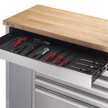 A close-up shows a partially extended drawer of a stainless steel rolling workbench. The drawer is lined with a black mat and contains various hand tools including pliers, a hammer, an adjustable wrench, and several screwdrivers with red handles.