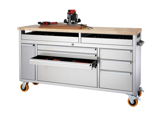 A wide shot shows a stainless steel rolling workbench with a light-colored wooden top. The workbench features multiple drawers and a cabinet, some of which are partially open revealing tools inside.