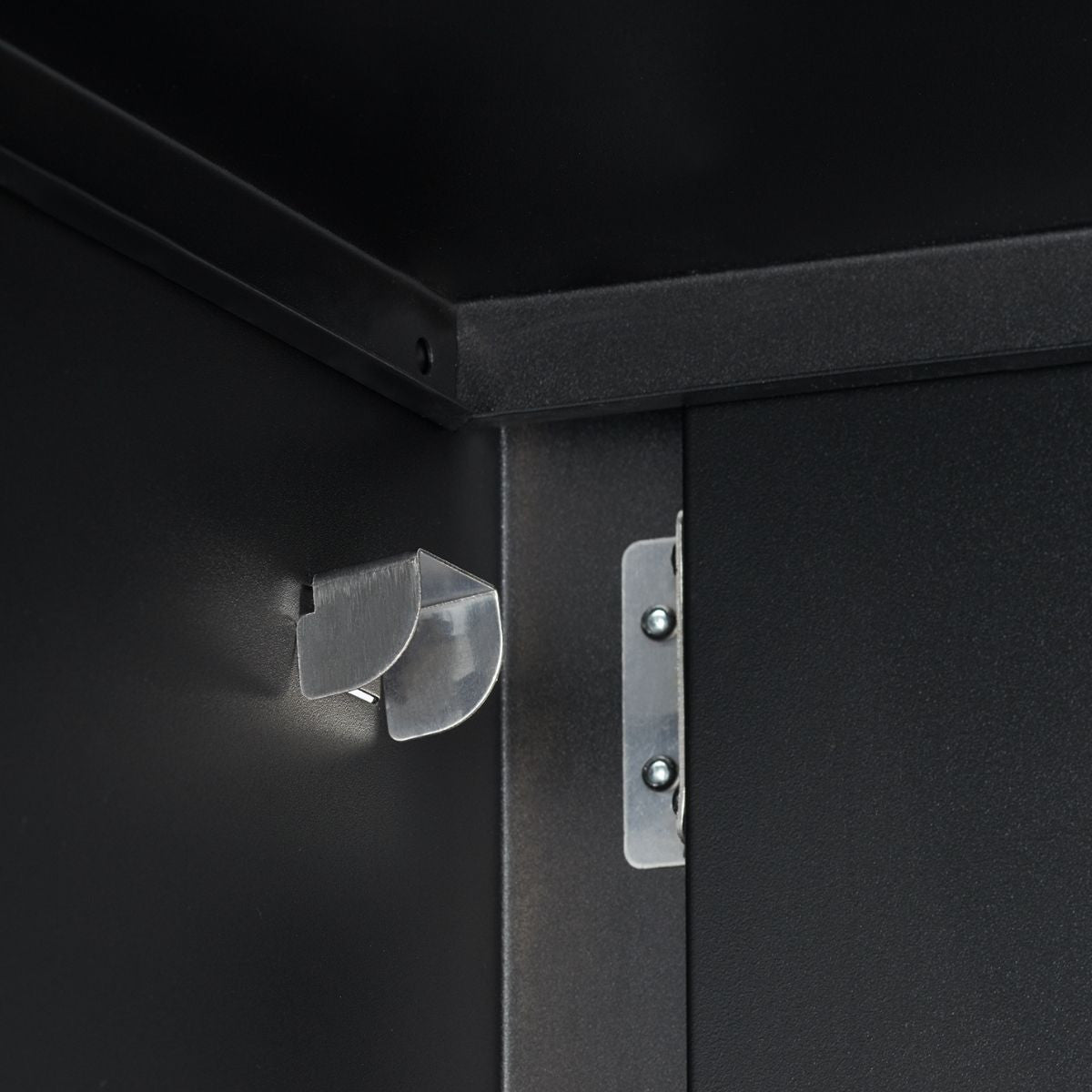 A close-up shot shows the interior of a black metal cabinet. Visible are a silver magnetic door catch on the left side panel and a silver hinge attached to the right side of the cabinet opening.