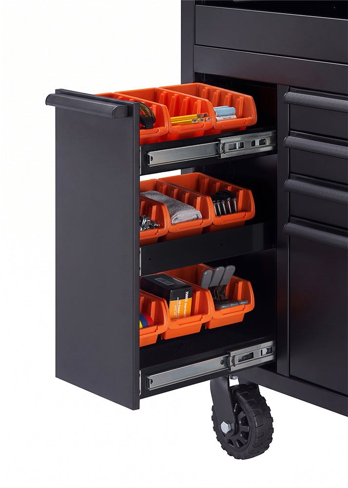 A close-up shot focuses on the pull-out side cabinet of a black tool workbench mounted on a heavy-duty caster wheel. The cabinet features three tiers of smooth ball-bearing slides holding vibrant orange organizer bins filled with small hardware, batteries, and supplies.