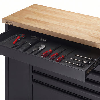 A close-up view highlights the open top-left shelf of a black tool workbench beneath a butcher-block wood top. The lined drawer interior displays neatly organized hand tools, including a hammer, pliers, and several screwdrivers.