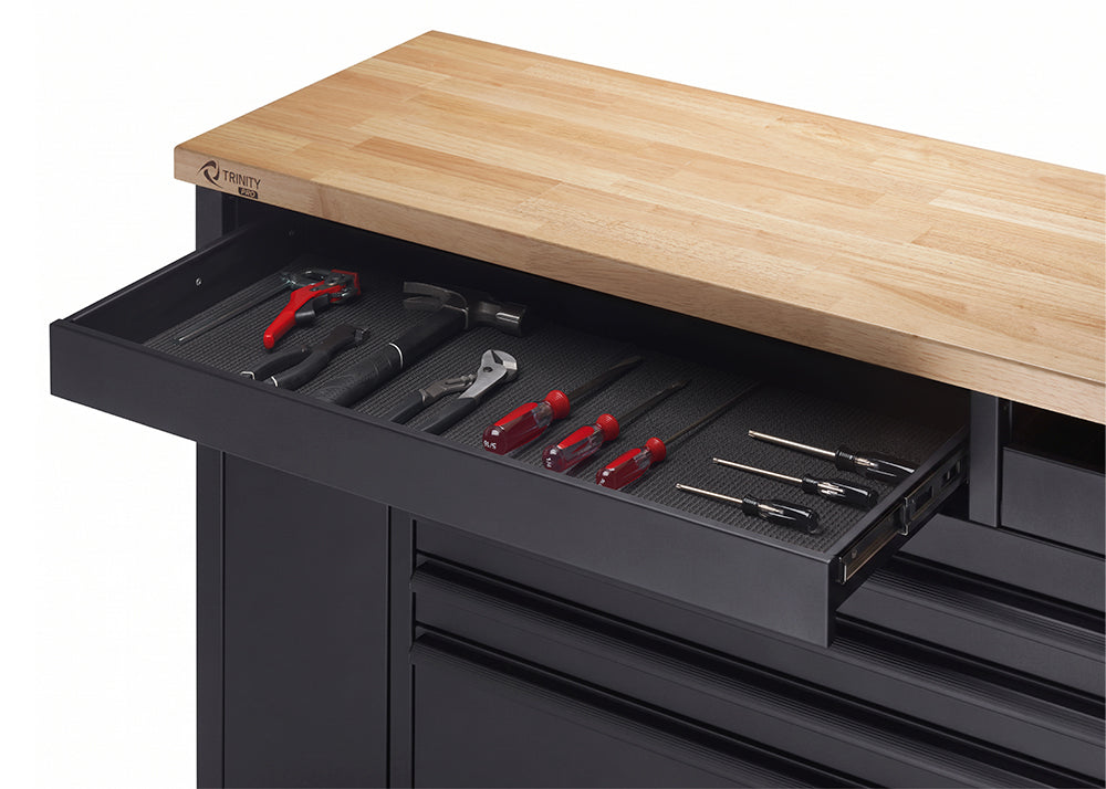 A close-up view highlights the open top-left shelf of a black tool workbench beneath a butcher-block wood top. The lined drawer interior displays neatly organized hand tools, including a hammer, pliers, and several screwdrivers.