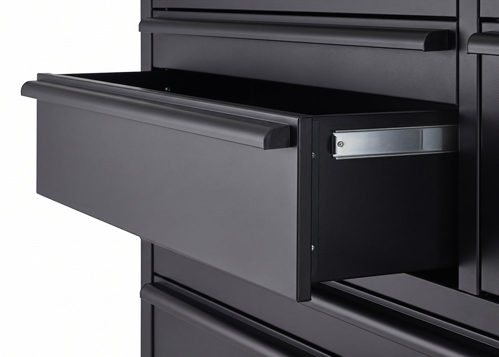 A close-up view focuses on an open drawer of a matte black tool chest, extending smoothly on a metal ball-bearing slide. The wide, deep drawer features a full-length black aluminum pull handle along its top front edge.