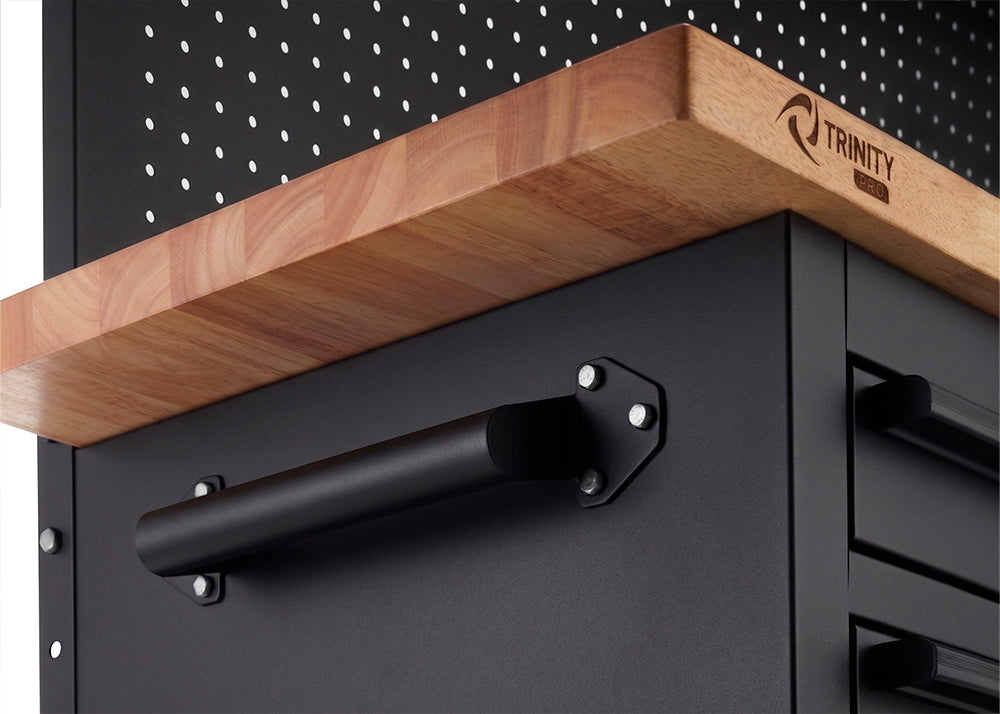 A close-up view highlights a sturdy, matte black handle bolted to the side of a black tool cabinet. Just above the handle, the edge of a thick wooden workbench top features the branded "TRINITY PRO" logo.