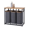 A three-compartment laundry sorter with a sturdy black metal frame, dark gray fabric hampers with wooden rims, and a light-colored wooden top surface. The top holds a detergent bottle and a glass jar with wooden clothespins.