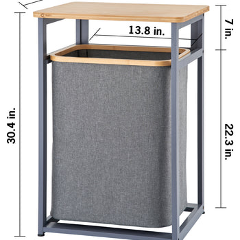 A dark gray metal hamper frame topped with a light wood table surface contains a removable gray fabric laundry bin inside. Dimension markings show overall outer measurements of 21.1 inches wide, 17.3 inches deep, and 30.4 inches in total height, with additional callouts specifying a 7-inch top opening clearance, a 13.8-inch inner width gap, and a 22.3-inch tall hamper section.