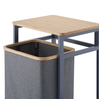 A close-up view demonstrates the gray fabric hamper bag pulled forward out of its dark gray metal frame, showcasing its wooden top rim. Above the hamper, a smooth wooden tabletop rests on the frame against a clean white background.