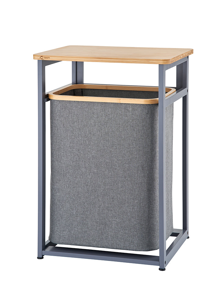 A standalone laundry hamper unit features a dark gray metal frame and a smooth wooden tabletop. Suspended within the frame is a removable gray fabric hamper bag with a wooden trim around the top rim.