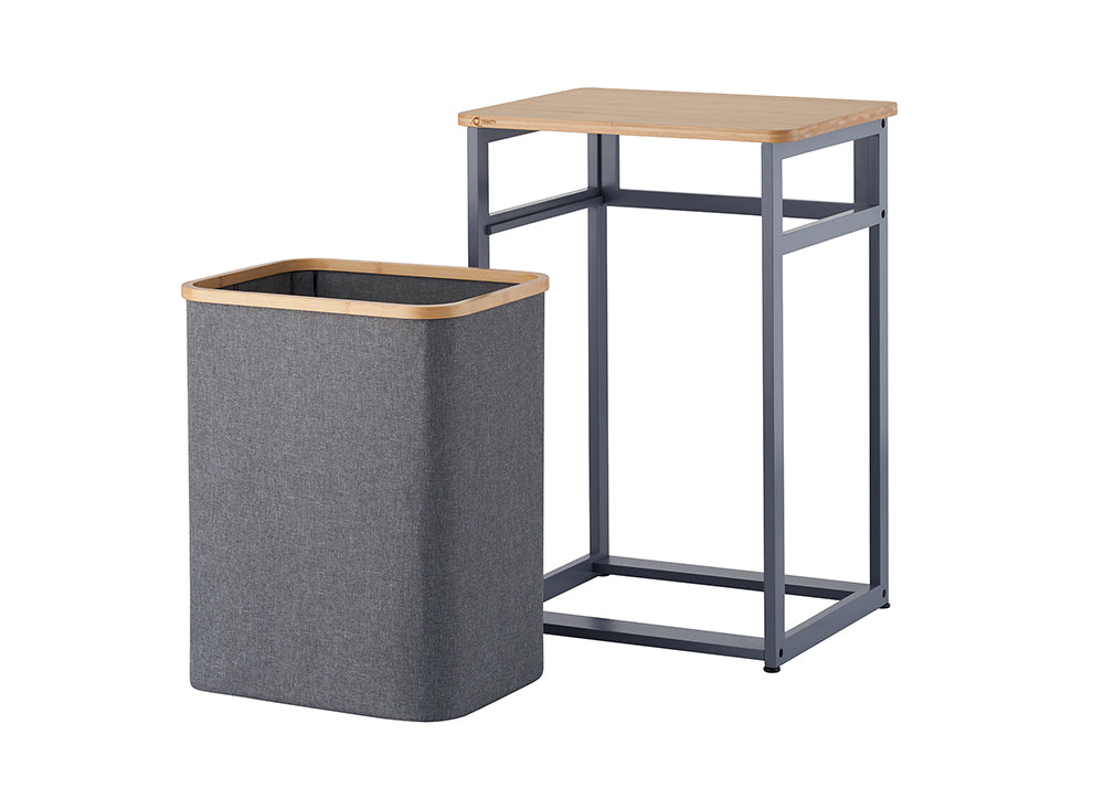 A gray fabric laundry hamper with light wood trim stands detached beside its dark gray metal frame. The frame features an open base design topped with a matching wooden tabletop on a plain white background.