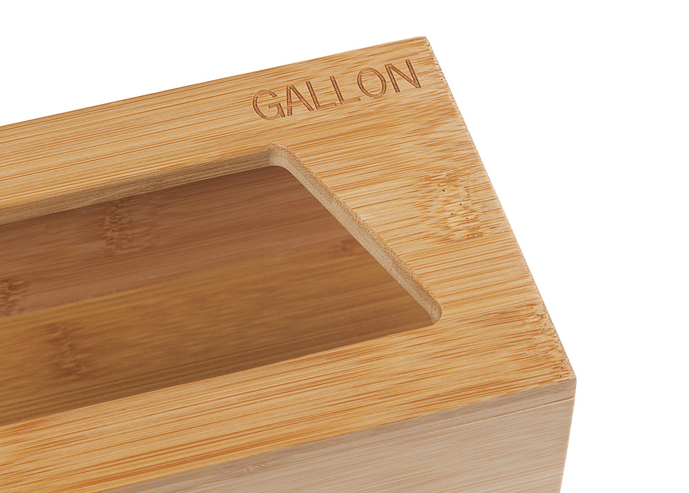 A close-up shot shows a light-colored wooden box with a rectangular cutout on top. The word "GALLON" is engraved into the wood near the top right corner of the box.