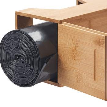 A close-up shows a roll of black plastic bags inside a light brown bamboo dispenser. The dispenser has a partially open sliding door with a vertical groove for easy gripping.