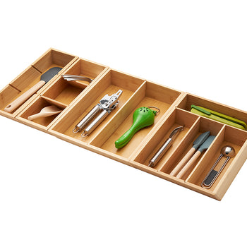 A high-angle shot of a rectangular, adjustable bamboo drawer organizer filled with various kitchen utensils. The organizer has five main compartments, with an additional smaller compartment on the far left.
