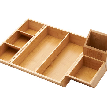A close-up shot of a light wood, possibly bamboo, desk or drawer organizer. The organizer has multiple rectangular compartments of various sizes, with an attached smaller caddy on the right.