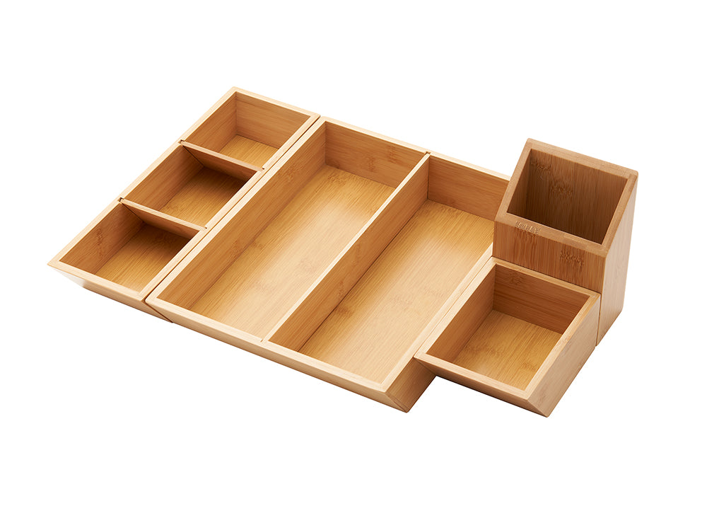 A close-up shot of a light wood, possibly bamboo, desk or drawer organizer. The organizer has multiple rectangular compartments of various sizes, with an attached smaller caddy on the right.