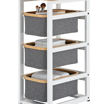 A white-framed storage cart features a light-wood top and three tiers of gray fabric bins with matching wood trim. The bins are shown holding bathroom essentials like makeup brushes and folded white towels.