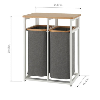A two-compartment laundry hamper with a light wood top and a white metal frame. The hamper has two gray fabric bins for sorting laundry, and its dimensions are 30.43 inches high, 24.57 inches wide, and 17.32 inches deep.