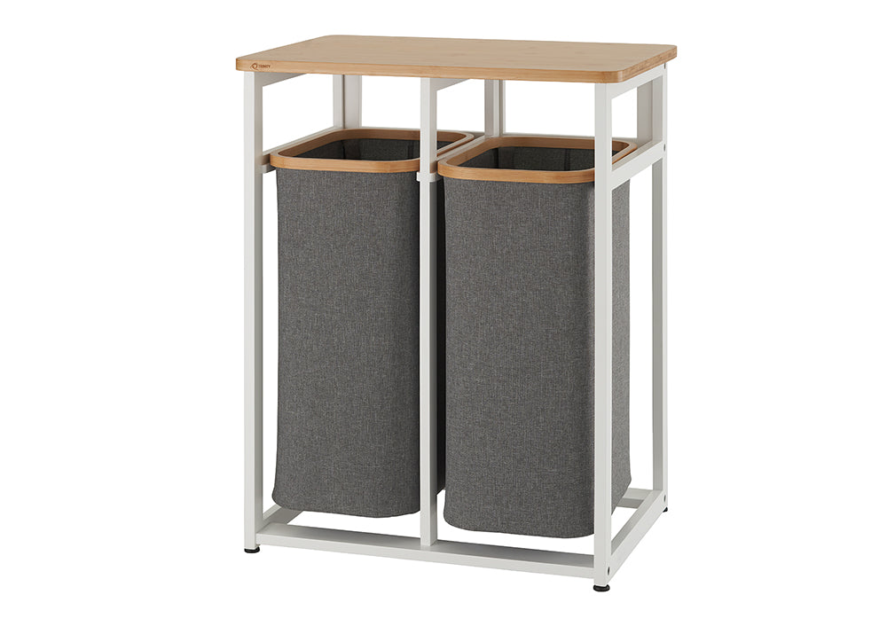 A tall, narrow laundry hamper with two separate gray fabric baskets held within a white metal frame. The top of the frame is a light-colored wood surface that can be used for folding clothes or other storage.