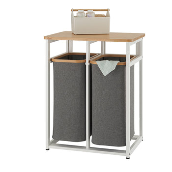 A modern, minimalist laundry sorter with a white metal frame and a light wood top. It features two removable grey fabric hampers, with a small organizer basket on the top shelf.