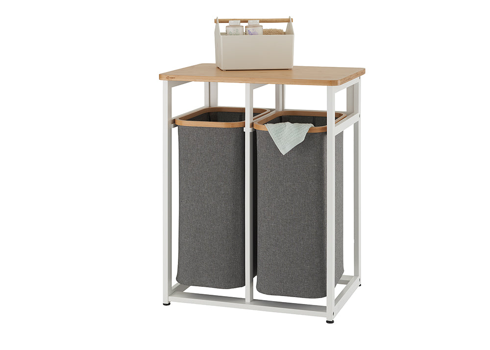 A modern, minimalist laundry sorter with a white metal frame and a light wood top. It features two removable grey fabric hampers, with a small organizer basket on the top shelf.