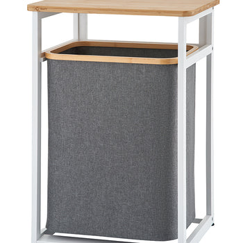 A minimalist laundry hamper stand features a white metal frame, a flat wooden tabletop, and a removable dark grey fabric basket. The product is shown completely empty against a plain white background.