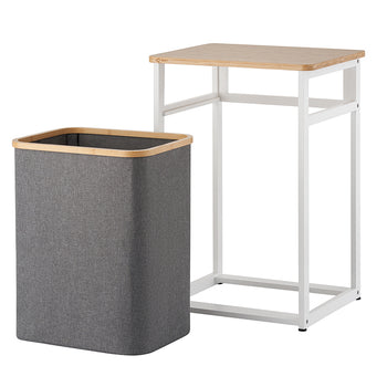 A dark gray fabric hamper with a bamboo rim sits detached beside its white metal and wood frame stand. The isolated product view demonstrates how the fabric bin easily slides out from under the table unit against a plain white background.