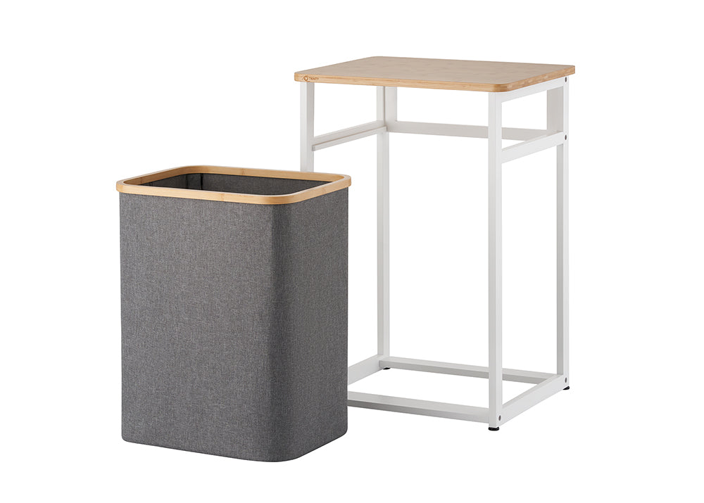 A dark gray fabric hamper with a bamboo rim sits detached beside its white metal and wood frame stand. The isolated product view demonstrates how the fabric bin easily slides out from under the table unit against a plain white background.