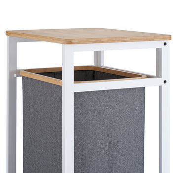 A close-up view highlights the top section of a laundry hamper stand, showing its smooth, light wooden tabletop and sturdy white metal frame. Suspended below the tabletop is a dark grey fabric hamper lined with a matching natural wood trim at the top opening.