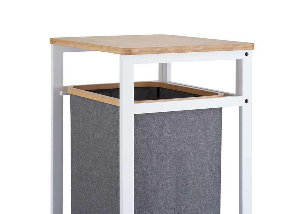 A close-up view highlights the top section of a laundry hamper stand, showing its smooth, light wooden tabletop and sturdy white metal frame. Suspended below the tabletop is a dark grey fabric hamper lined with a matching natural wood trim at the top opening.
