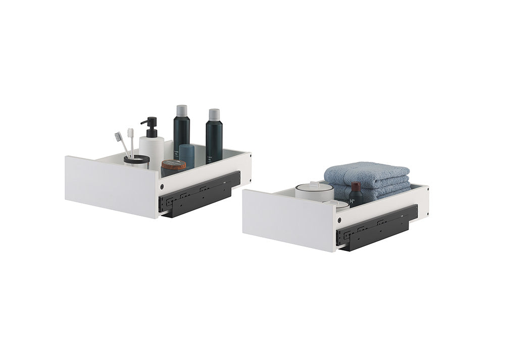 Two white, pull-out organizer drawers with black metal sliding hardware are displayed side-by-side against a plain white background. The left drawer holds toiletries including toothbrushes, soap dispensers, and dark bottles, while the right drawer contains folded blue towels and small bathroom containers.