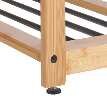 A close-up of the bottom corner of a light brown, wooden shoe rack. The rack is made of what appears to be bamboo with black metal rods forming the shelves and has a black, adjustable foot on one of the legs.