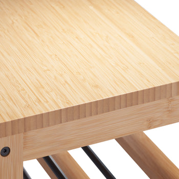 A close-up shot of a light-colored wooden bench or table, revealing its natural grain and texture. The wood appears to be bamboo, with visible joints and black screws at the corners.