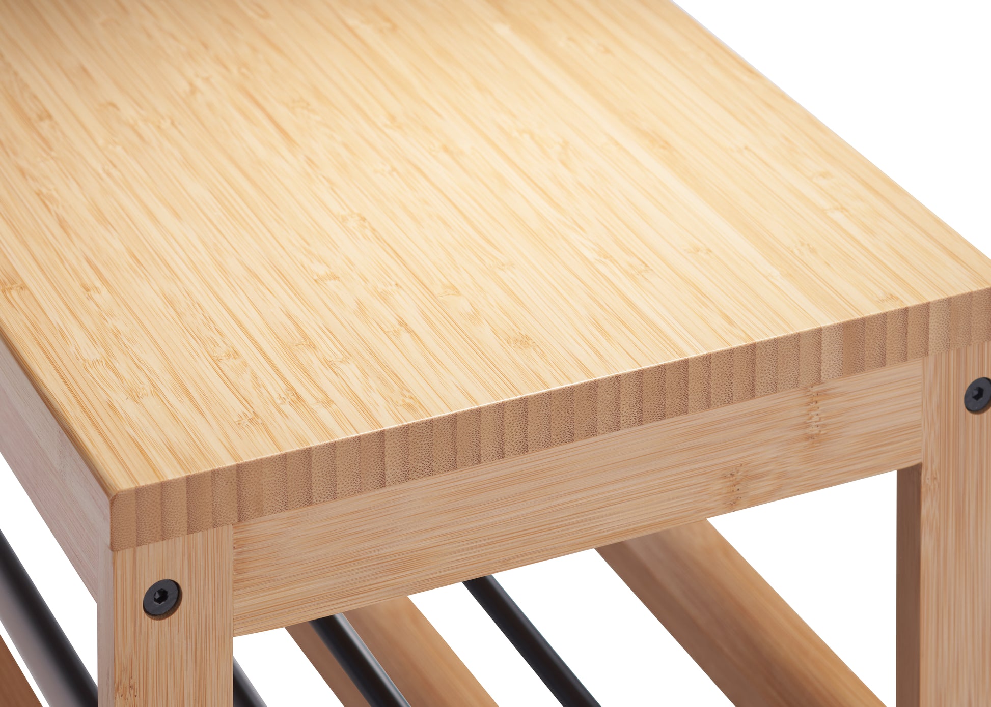 A close-up shot of a light-colored wooden bench or table, revealing its natural grain and texture. The wood appears to be bamboo, with visible joints and black screws at the corners.