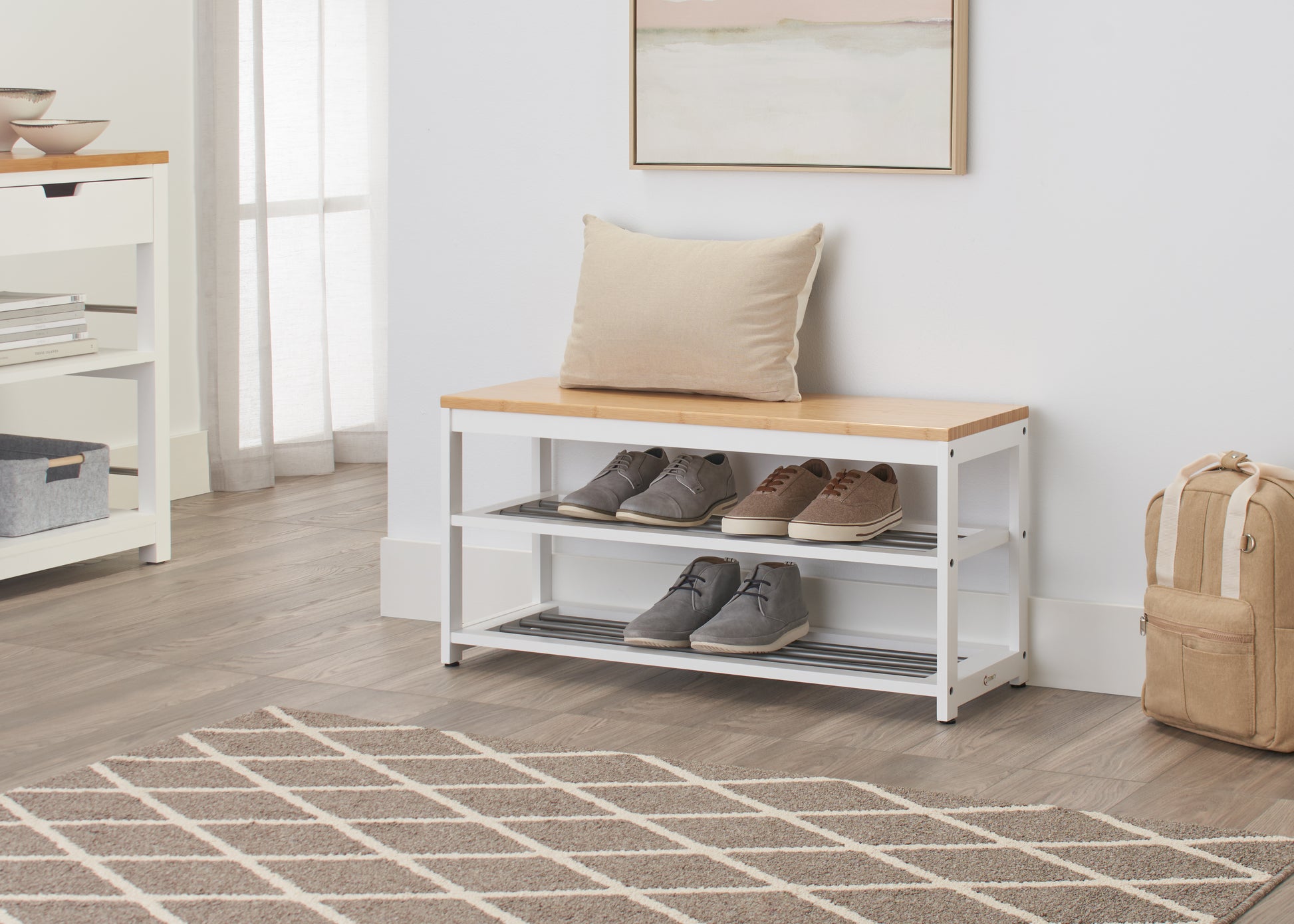 A shoe storage bench is placed in a light-filled entryway. The bench has a light wood top and two white metal racks below holding several pairs of shoes.