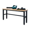A workbench with a light-colored wooden top and black metal legs stands against a white background. Several power tools, including a teal leaf blower and a battery charger with batteries, rest on the tabletop.