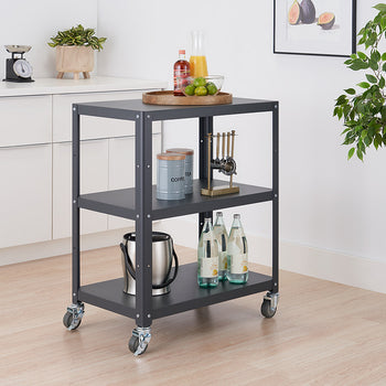 A gray metal utility cart with three shelves on wheels is positioned in a kitchen setting. The cart holds various items, including bottles, a bucket, and a tray with food.