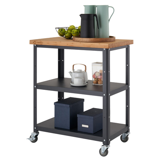 A kitchen cart with a light wood butcher block top, two dark gray metal shelves, and wheels is shown against a white background. The cart is styled with a tray, pitchers, fruit, a teapot, and storage boxes.