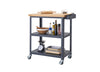 A dark gray Trinity 32" Bamboo Top Kitchen Cart on wheels is shown with a rolling pin on its bamboo top. The two lower shelves hold various kitchen items, including a bowl, bottles of oil, spices, a kitchen scale, and two baking pans.