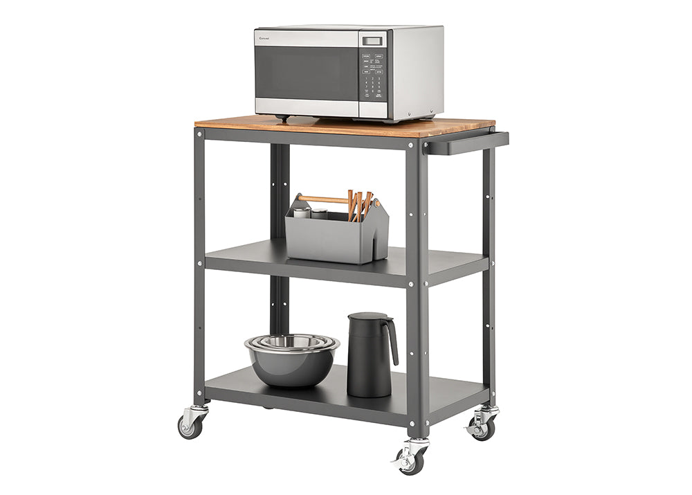 A three-tiered rolling utility cart with a dark gray metal frame and a light wood top shelf. A stainless steel microwave sits on the top, and the two lower shelves hold various kitchen items like bowls, a thermos, and a utensil caddy.