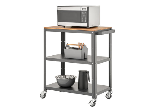 A three-tiered rolling utility cart with a dark gray metal frame and a light wood top shelf. A stainless steel microwave sits on the top, and the two lower shelves hold various kitchen items like bowls, a thermos, and a utensil caddy.